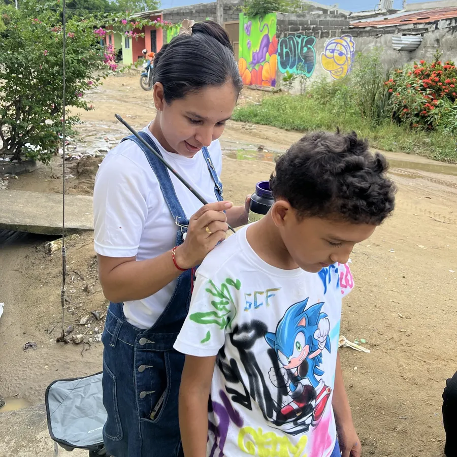 Dianis pintando la camiseta de un niño en una jornada de murales en el barrio