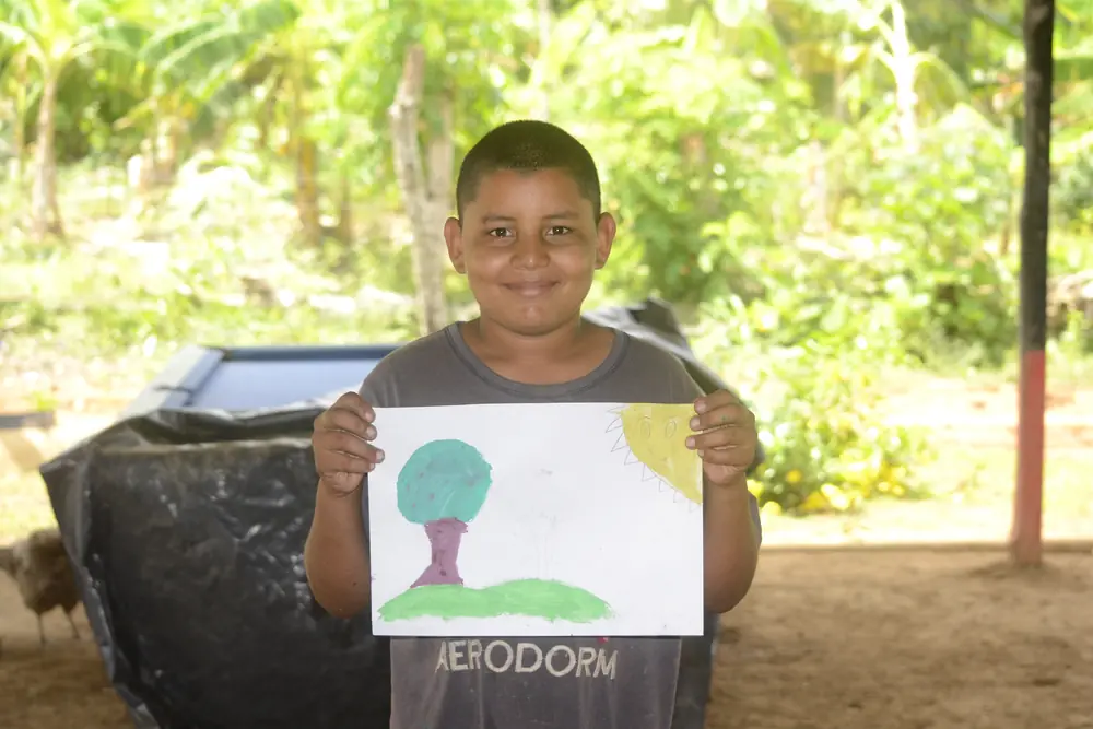 Un niño muestra el árbol que dibujó y pintó en el taller