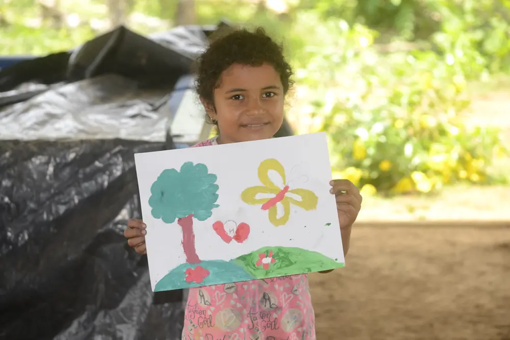 Una niña muestra su dibujo de un árbol y una mariposa